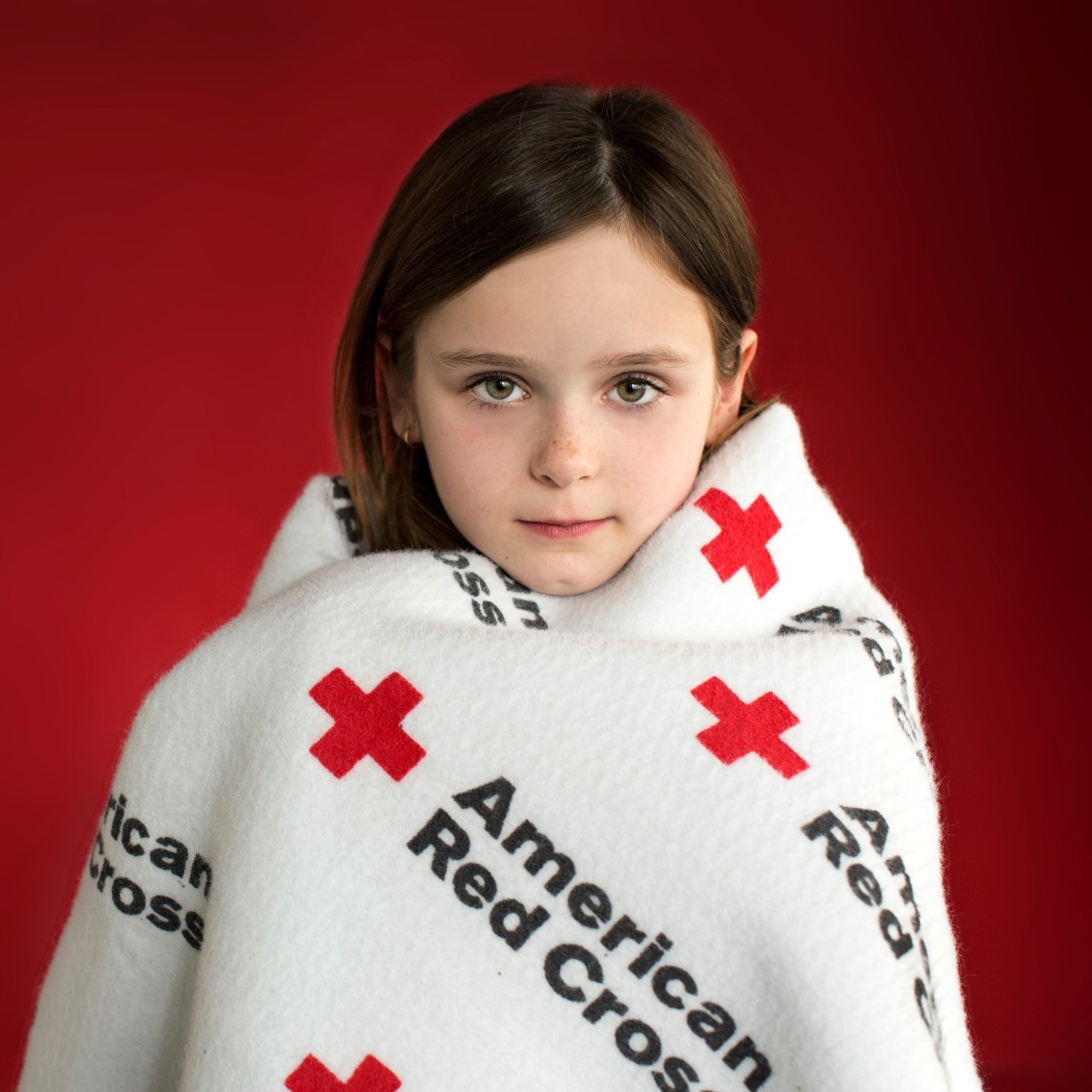 Young girl wrapped in a Red Cross blanket.