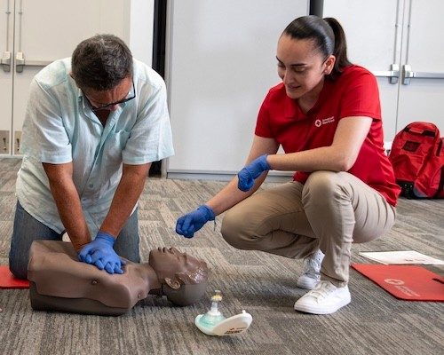 Red Cross instructor oversees CPR training as a man practices on a dummy