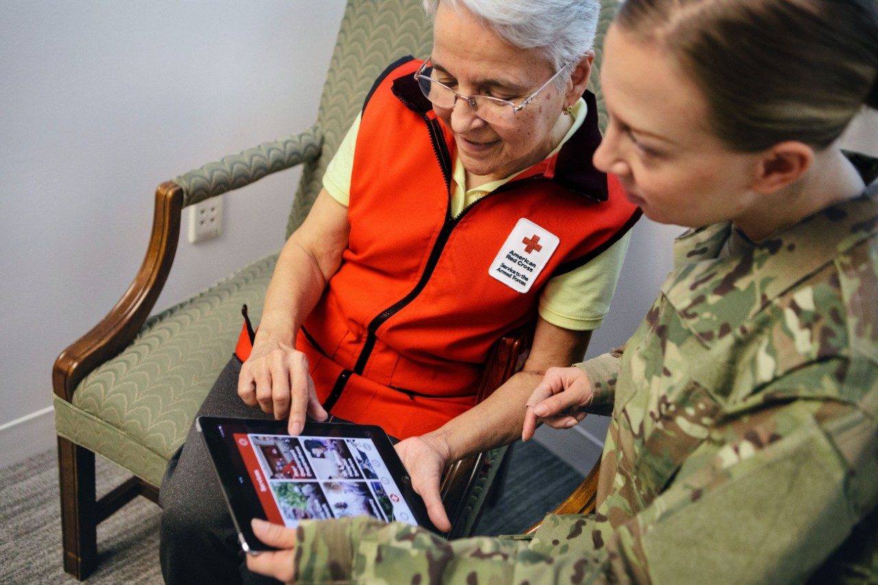 Red Cross volunteer looking at tablet with female military member