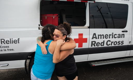 Two women hugging standing near Red Cross vehicle