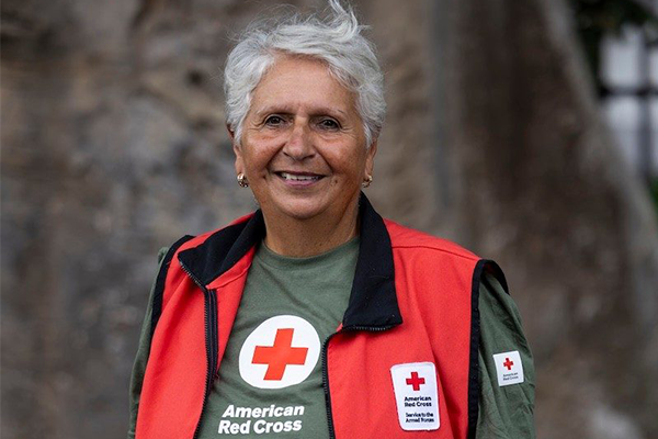 Carmen Hernandez, a women with short, white hair and tan skin smiles while wearing a Red Cross t-shirt and Red Cross Hero Care vest