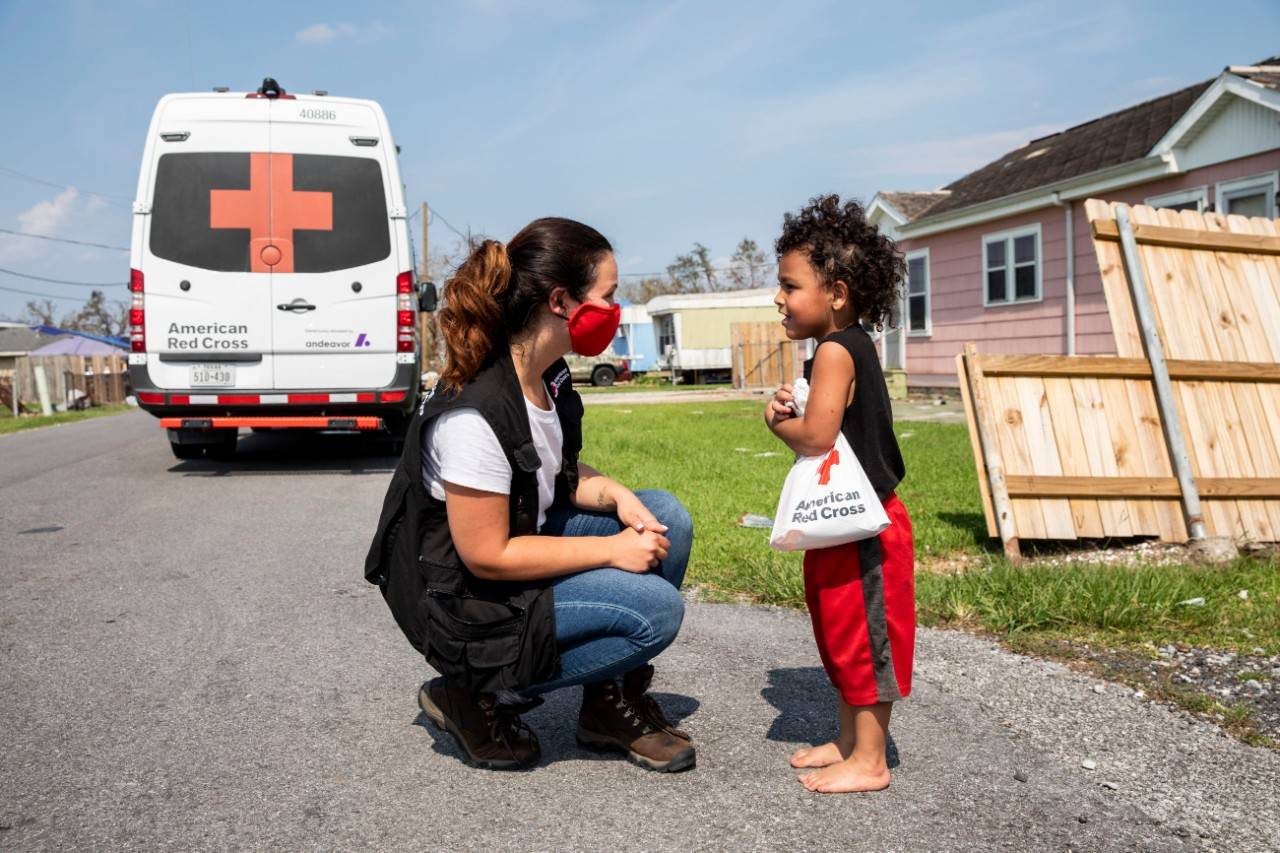 September 3, 2021. Larose, Louisiana. Stefanie Arcangelo of the American Red Cross shares a comfort kit and a smile with a child after Hurricane Ida left him, his three siblings and his mother, Yvonne Padilla Lucca without power and with damage to their home, in Larose, Louisiana on September 3, 2021. In some of the hardest hit parishes, like Larose, the Red Cross has emergency response vehicles circulating through accessible areas to distribute critical supplies including water, comfort kits and ready to eat meals. Photo by Scott Dalton/American Red Cross