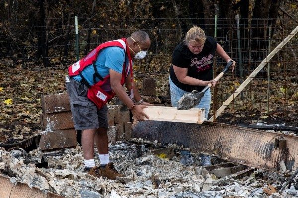 A Red Cross volunteer helps a homeowner sift debris after a wildfire