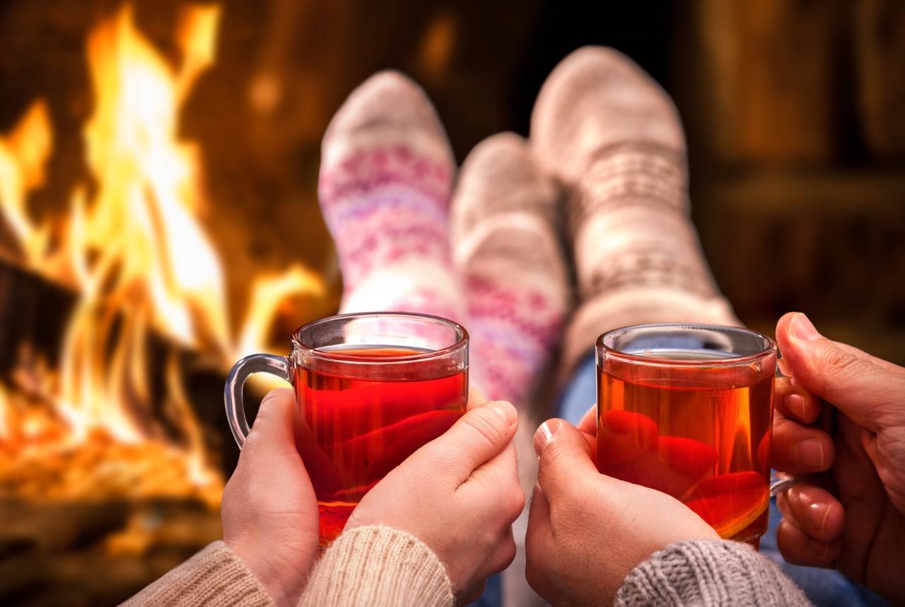 Couple relaxing with mulled wine at romantic fireplace on winter evening