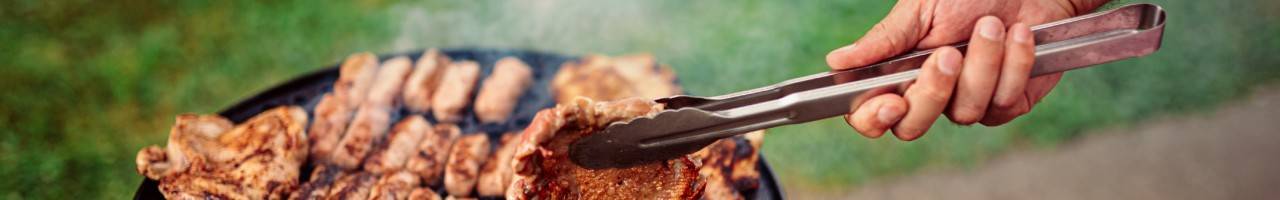 Hand holding tongs flipping meat on a grill