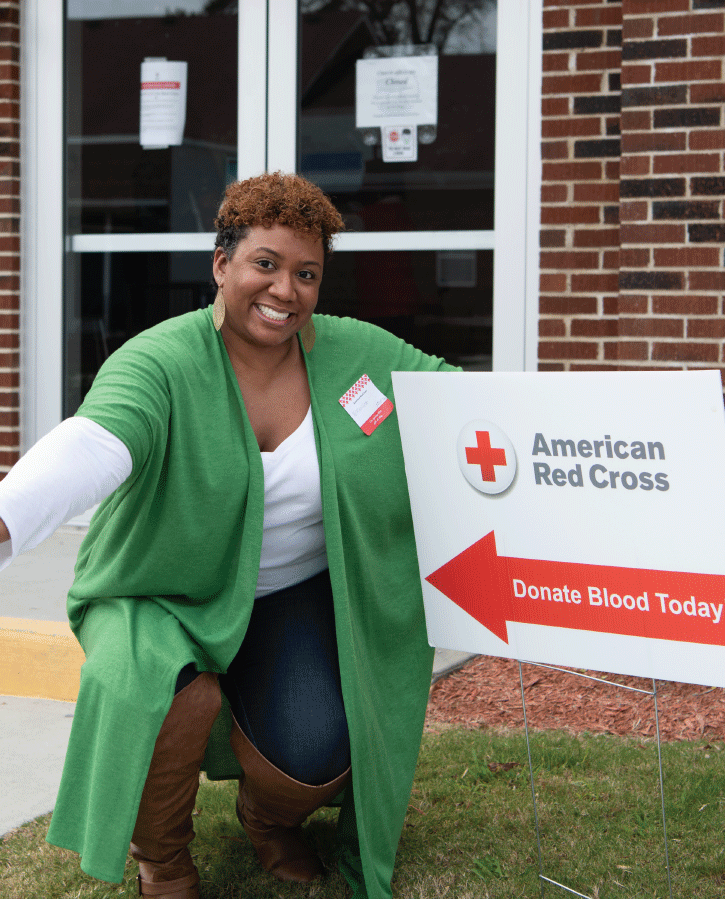 Woman squatting next to Red Cross blood drive sign smiling