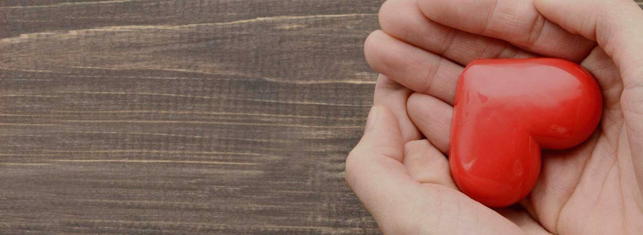 Hands holding a heart above a wood surface