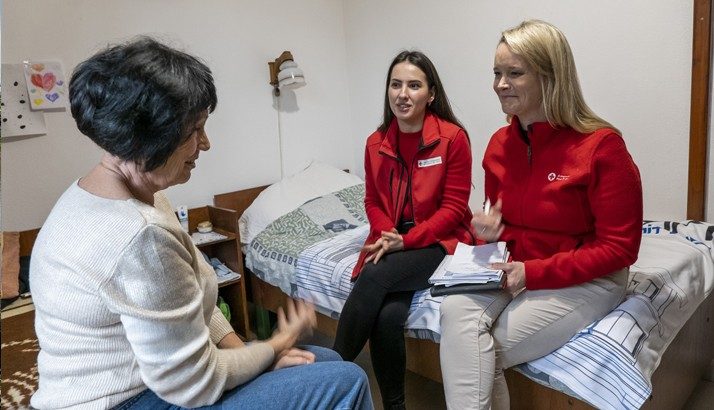 Two Red Cross volunteers are sitting down talking to a woman