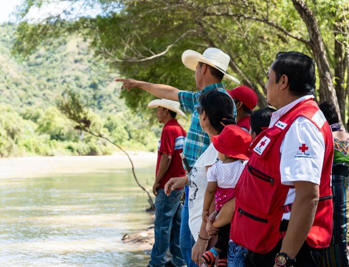 Red Cross volunteers and residents are standing on the bank of a river observing the damage