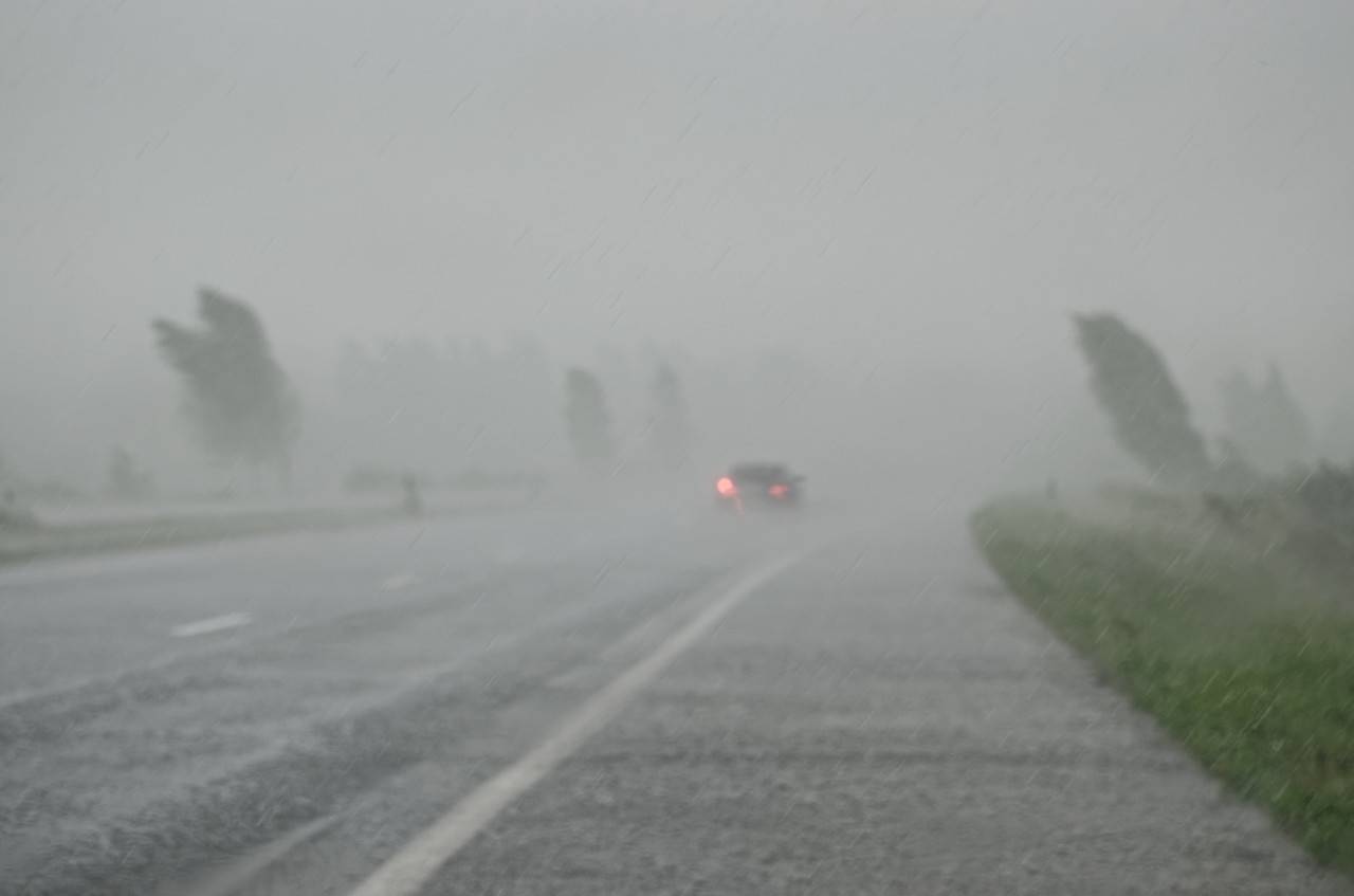 Heavy rainstorm with wind bending trees and poor visibility on motorway through car windscreen