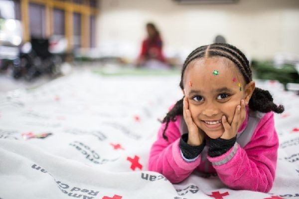 Child laying on Red Cross blanket, holding head with hands and smiling for camera.