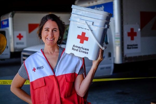 American Red Cross volunteer holding 5 gallon American Red Cross bucket on shoulder and smiling for picture.