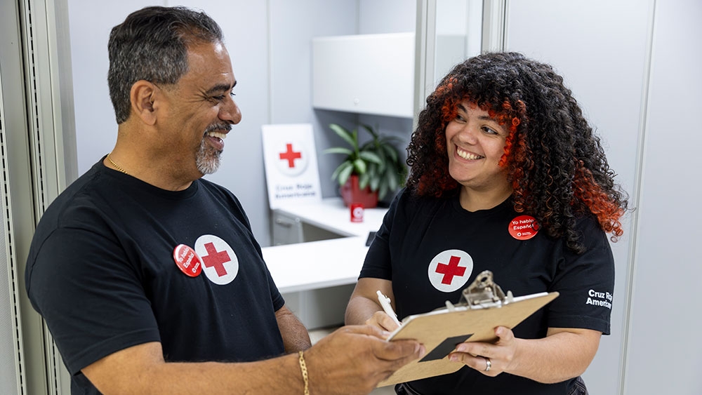 Un hombre y una mujer, voluntarios que llevan camisetas de la Cruz Roja, sostienen una carpeta con pinza.