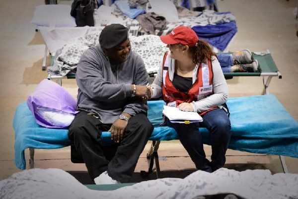 Red Cross volunteer and man sitting on cot shaking hands.