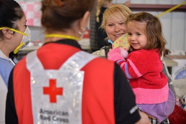 Red Cross volunteer looking at mother holding child.