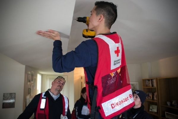 Red Cross volunteer installing a smoke alarm in ceiling of residence.