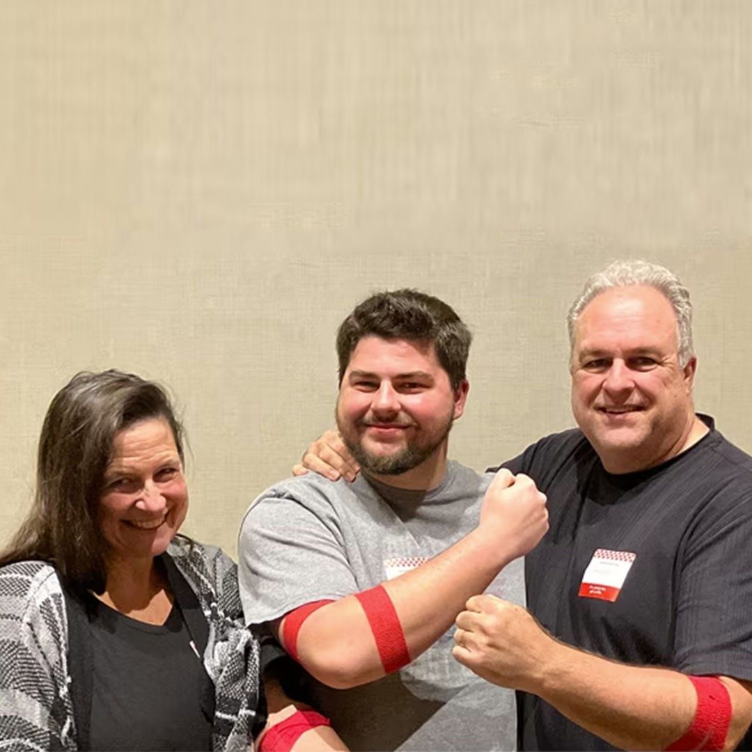 family of 3 smiling with red bands from giving blood