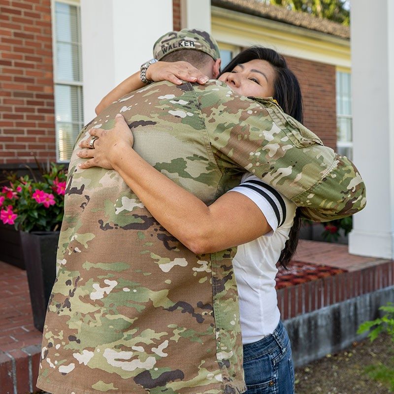 Military member in camo gear hugging a civilian.