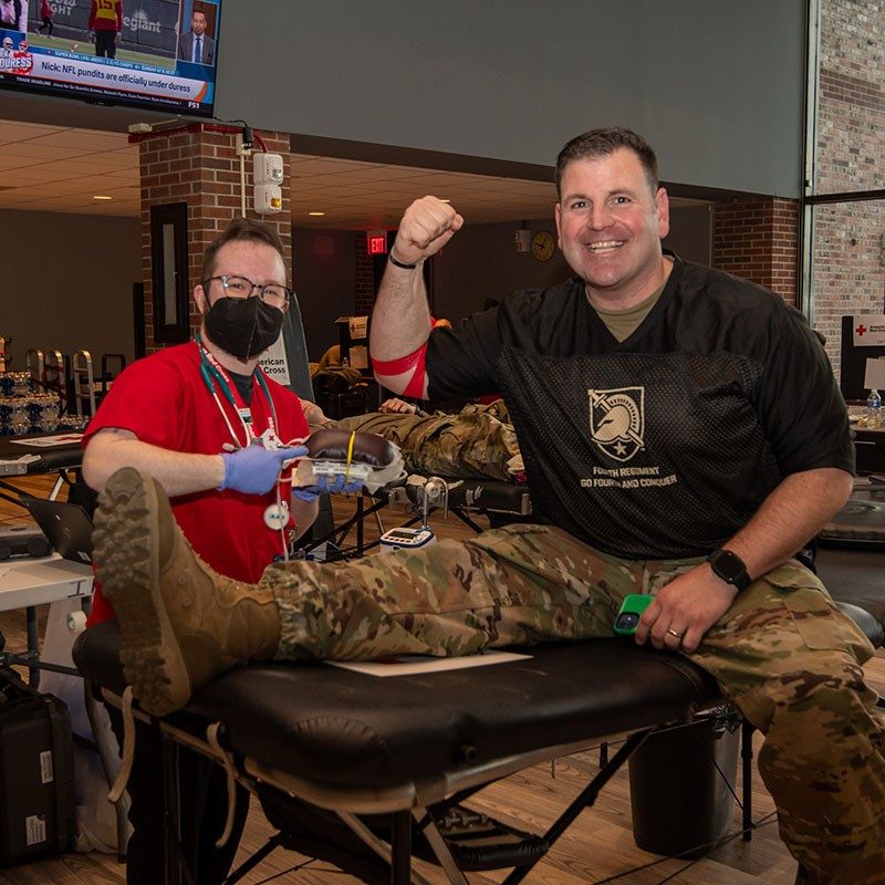 Red Cross nurse and service member with red bandage around arm after donating blood.