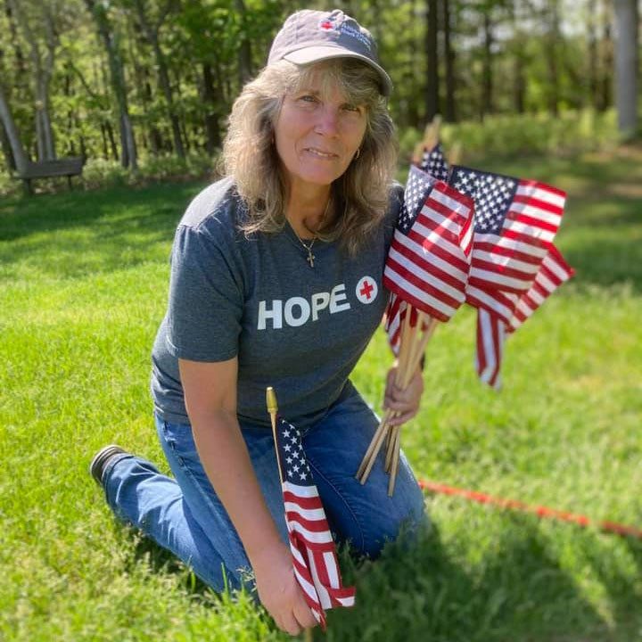 Doreen Brienza, wearing Red Cross shirt and hat, places flags and decorations at the Calverton National Cemetery.