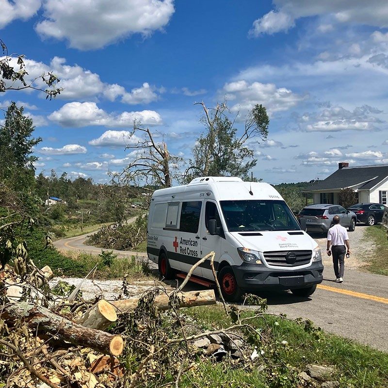 American Red Cross van on street next to home and cut up wood from fallen trees.
