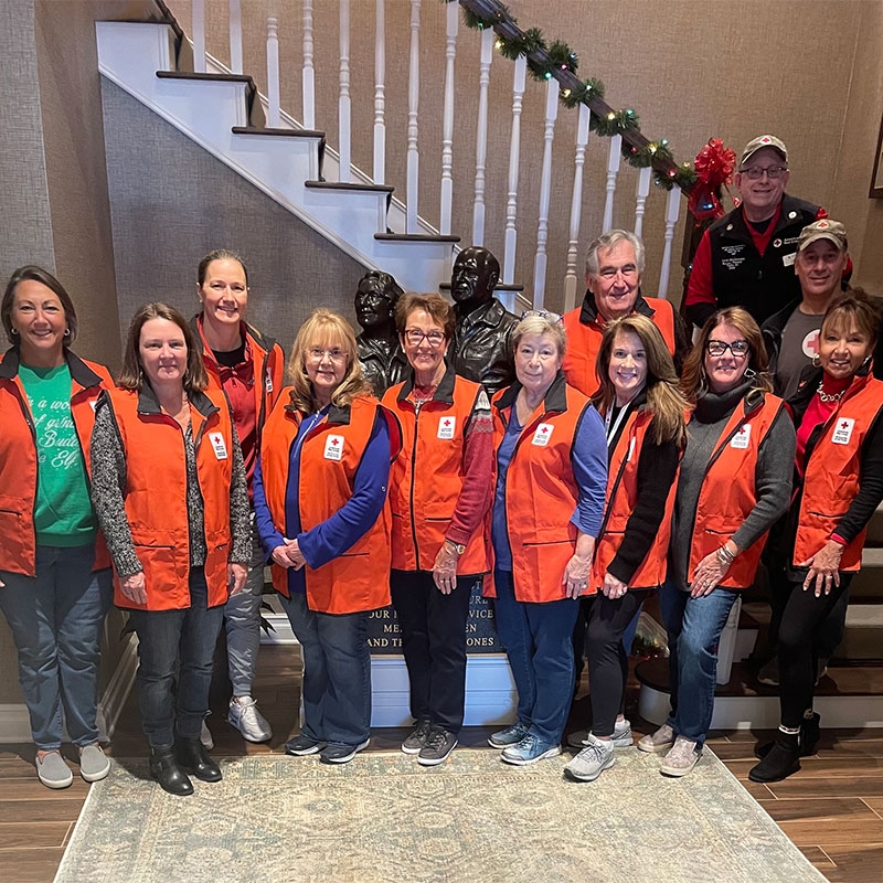 Group of Red Cross volunteers in Red Cross vests standing next to stairwell in the Fisher house.