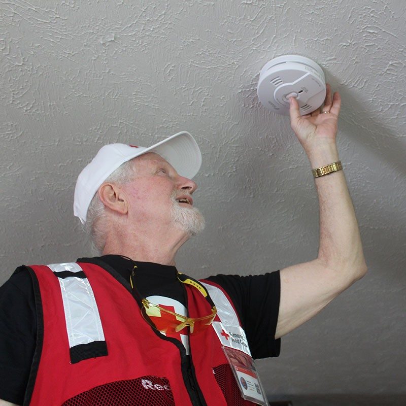 American Red Cross volunteer installing a smoke alarm on a ceiling.