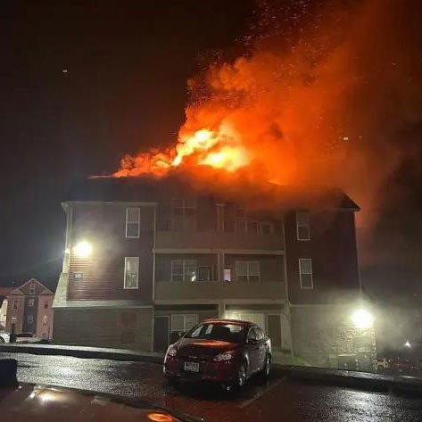 Apartment building on fire at night with a car parked in front.