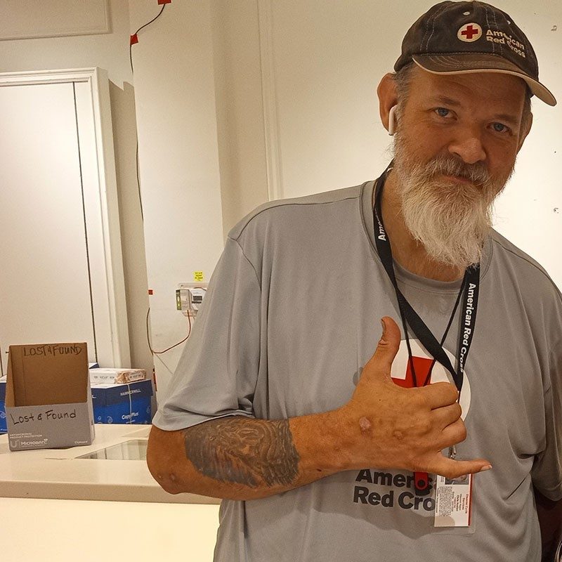 Chris Huston wearing an American Red Cross hat and shirt and giving the hang loose sign.