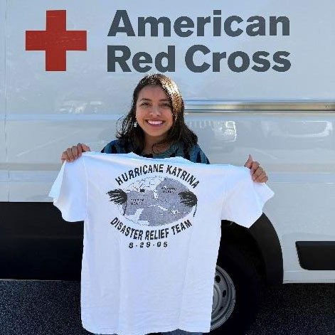 Rosy Crumpton standing next to a Red Cross van and holding up a t-shirt.