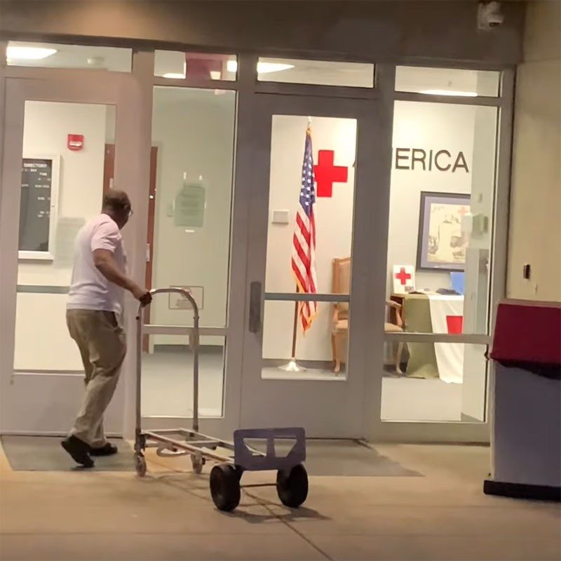 volunteer pulling a hand cart and walking into a red cross building.