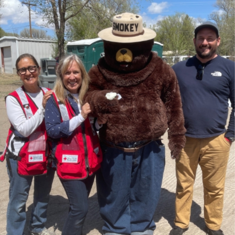 Three Red Cross volunteers standing next to Smokey the Bear mascot.