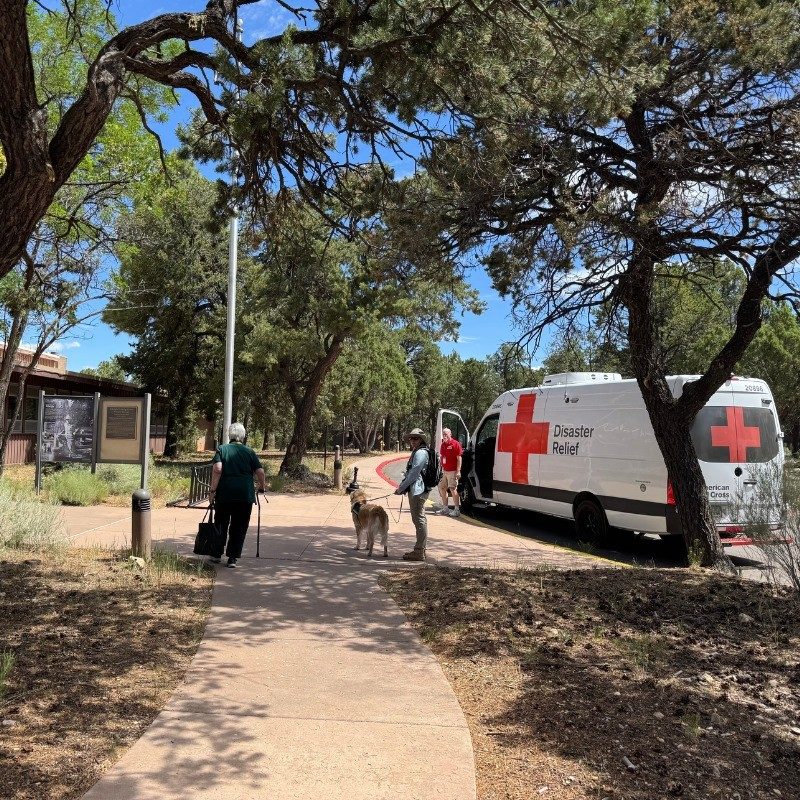Red Cross volunteer with dog on a leash talking to a client next to a Red Cross emergency response vehicle.