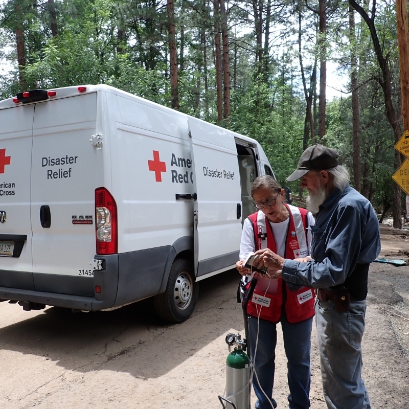 Red Cross volunteer in vest assiting client with an oxygen tank.
