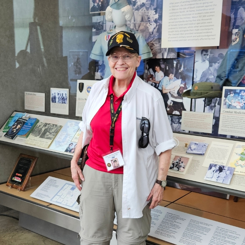 Shue smiling in veteran hat in front of the Military Women's Memorial.