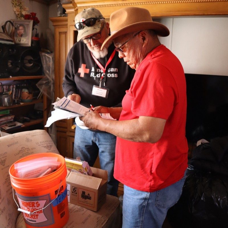 Two Red Cross volunteers assisting each other put up a smoke alarm in a home.