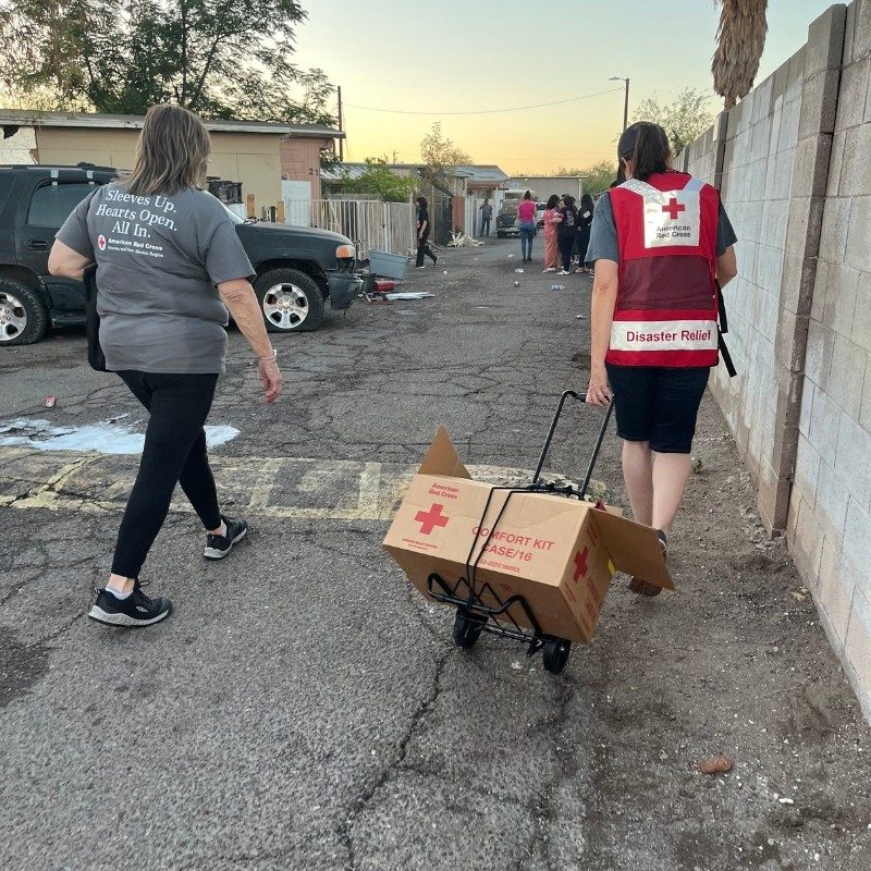 Two Red Cross volunteers carrying supplies towards a home.