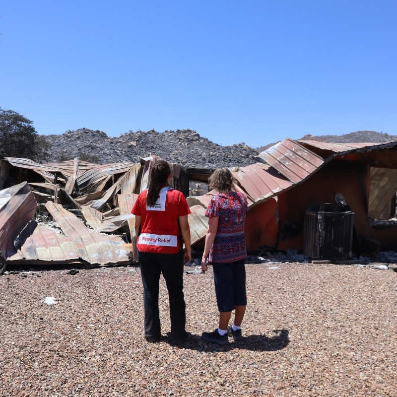 Red Cross volunteer standing next to client looking at damaged home.