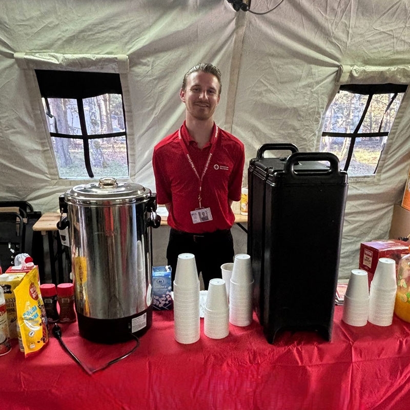 Red Cross volunteer behind a table with coffee and coffee cups.
