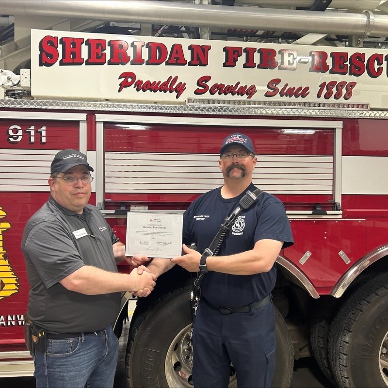 Person presenting an award to a firefighter in front of a fire truck.