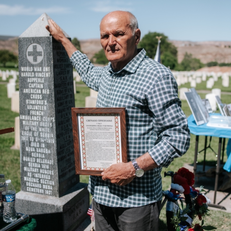 Man standing next to a headstone in a cemetrey.
