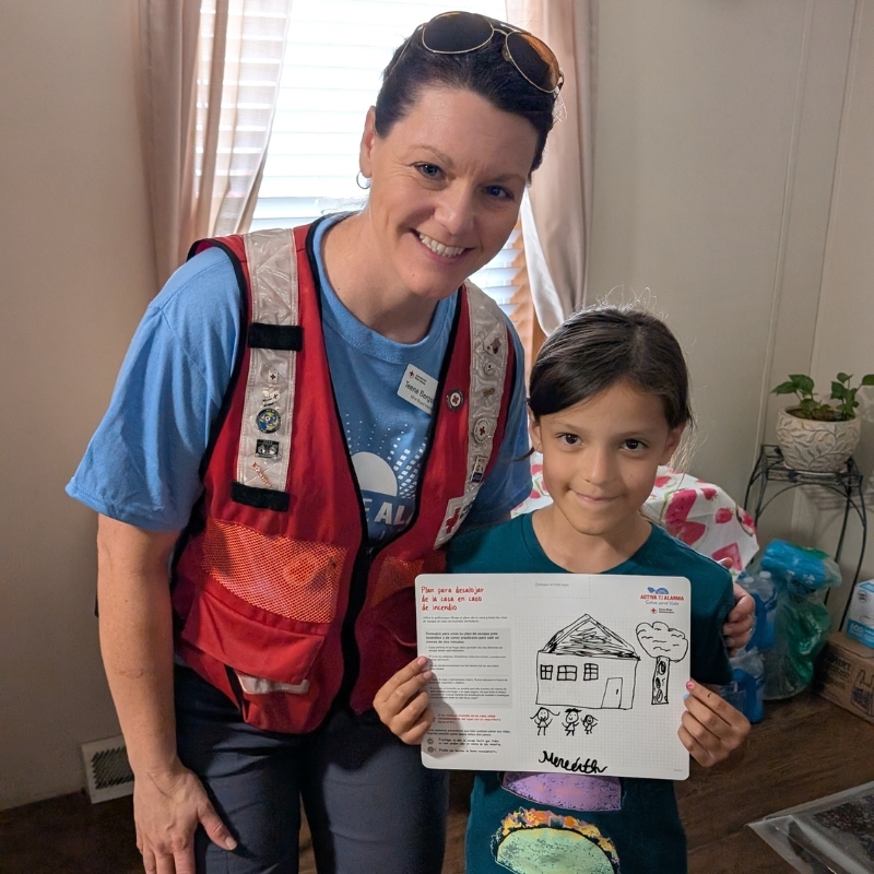 Red Cross volunteer standing next to a child holding a home fire safety plan. 