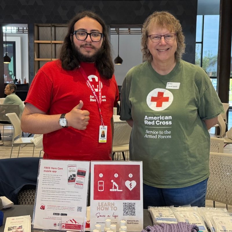 Two Red Cross volunteers standing at a table with Red Cross information on table.