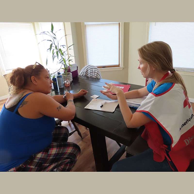 Red Cross volunteer and a local resident sitting at a kitchen table and talking with each other.