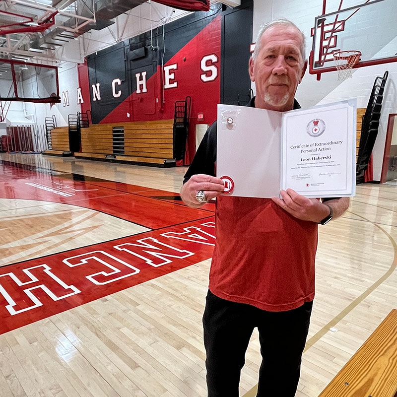 Leon Haberski standing in a basketball gym while showing his Red Cross Lifesaving Award.