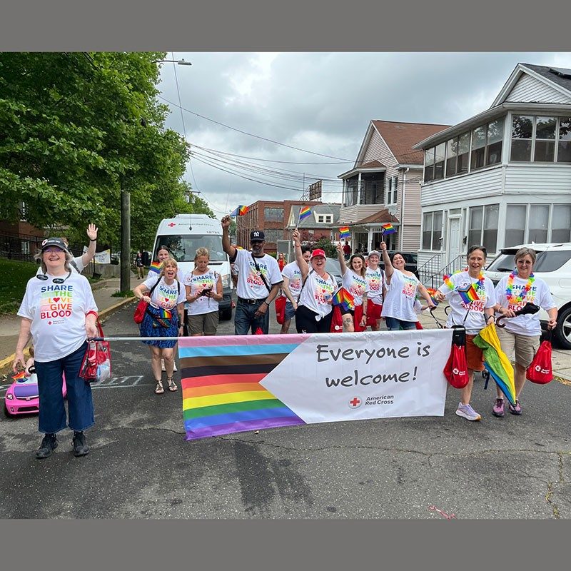 Group of people walking in a pride parade while holding a large banner that says, "Everyone is welcome!".