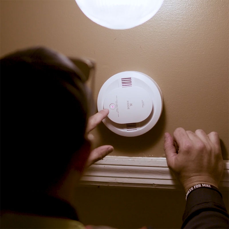 Red Cross volunteer testing a smoke alarm that's mounted on a wall.