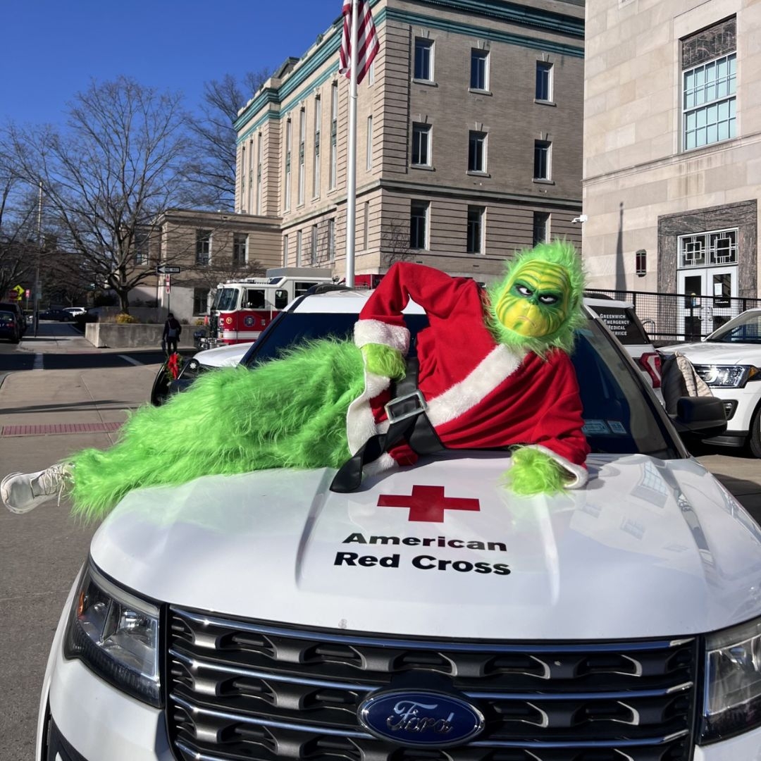 redcrosser in the grinch costume leaning on red cross vehicle