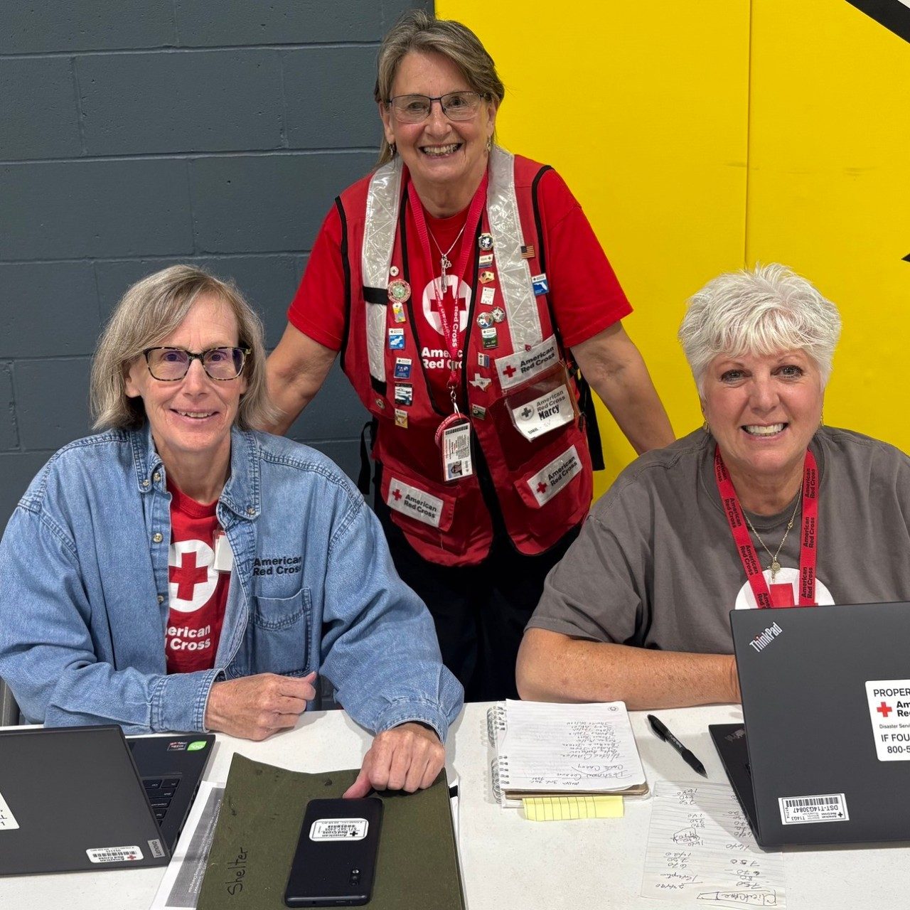 Three smiling Red Cross volunteers sitting at a desk.