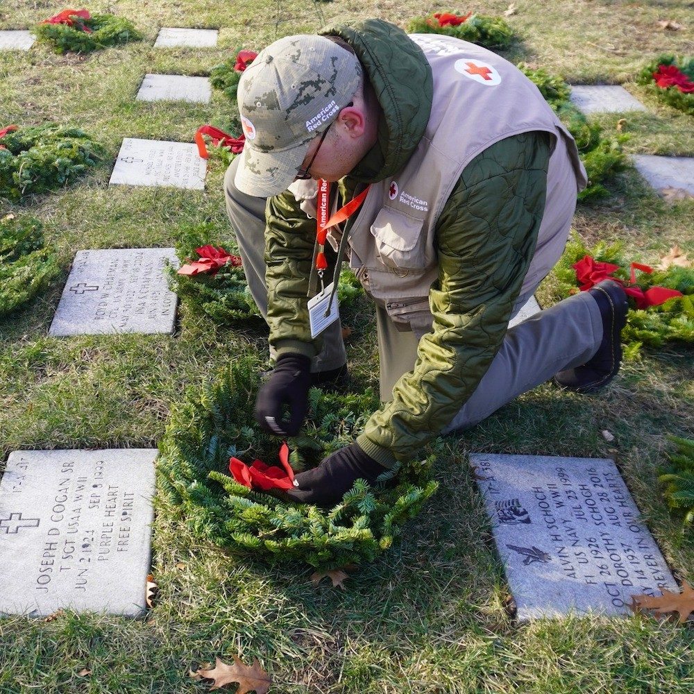 Red Cross volunteer laying wreaths at gravesites of veterans.